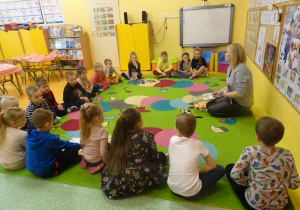 Grupa dzieci siedzi w półkolu wokół pani Magdaleny Siupy dyrektor Miejsko- Gminnej Biblioteki w Kleczewie, która prezentuje książki o tematyce świątecznej.